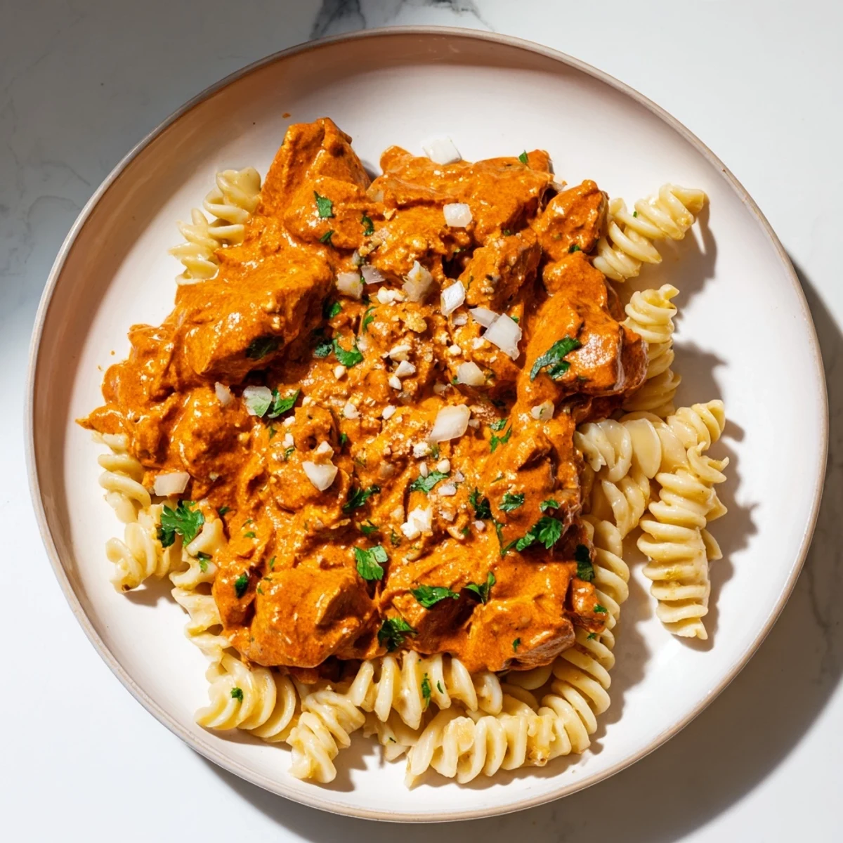 This close-up showcases a bowl of flavorful creamy chicken tikka masala pasta with fresh cilantro garnishing.