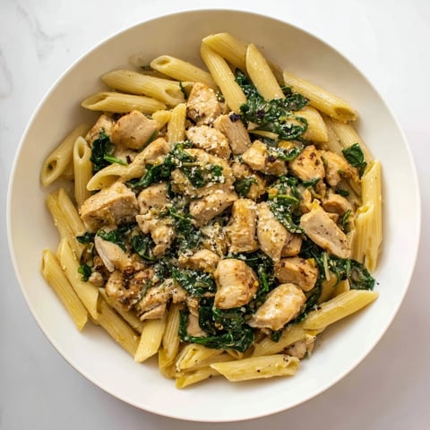 One-pot spinach and chicken pasta, steaming hot, with tender chicken and vibrant spinach visible.