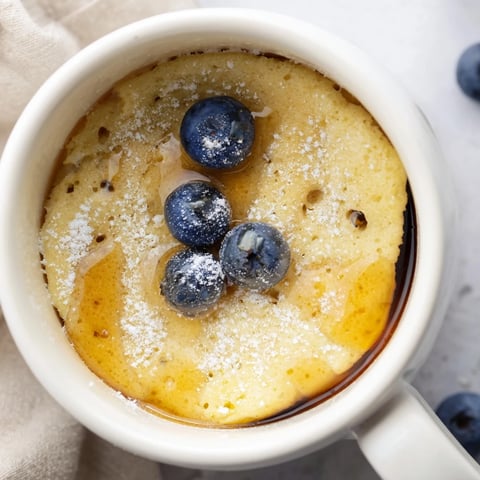 A mug overflowing with warm, golden Microwave Mug Pancakes, drizzled with sweet maple syrup.