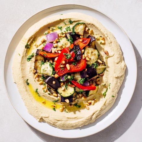 Vibrant hummus roasted veggies topped with charred vegetables and toasted pine nuts, a flavor explosion.