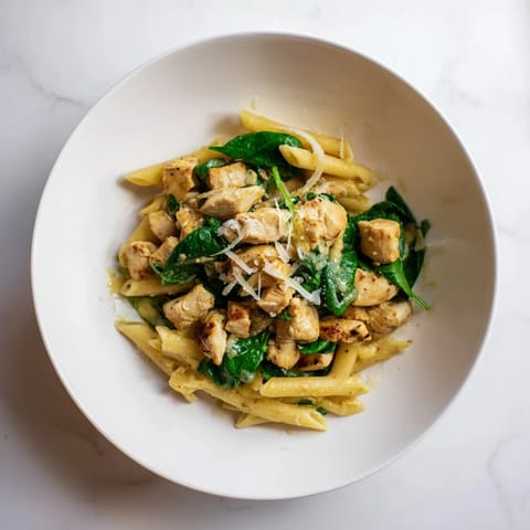 A close-up of a bowl of creamy one-pot spinach and chicken pasta, ready to eat with parmesan.