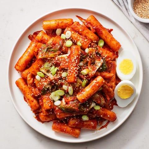 Chewy rice cakes simmer in a vibrant, sweet and spicy Korean tteokbokki sauce, served steaming hot in a bowl.