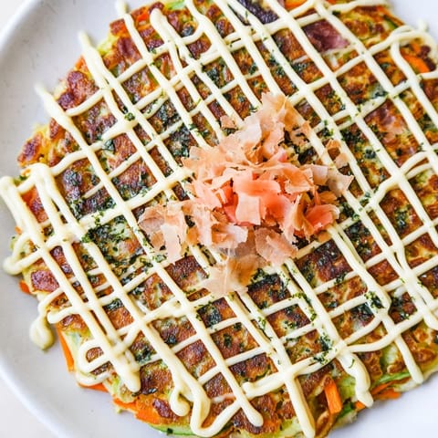Savory Japanese Okonomiyaki Pancakes served hot, drizzled with tangy sauce and finished with vibrant green onions.  