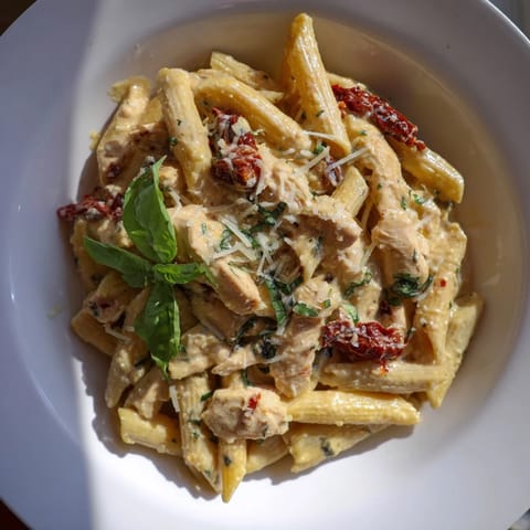 A comforting plate of Creamy Sun-Dried Tomato Chicken Pasta garnished with fresh basil and extra Parmesan, perfect for a cozy Italian-American dinner.