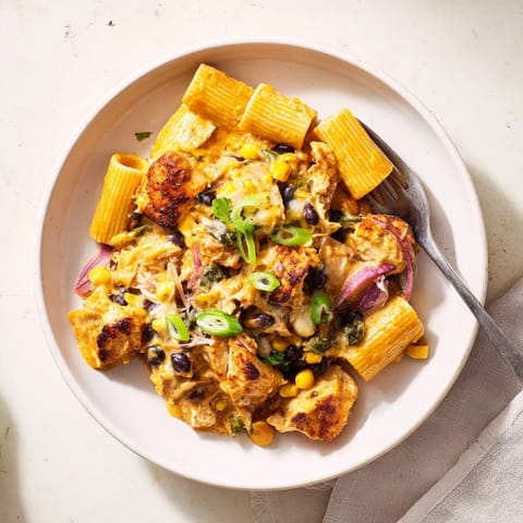 Crispy Chicken Burrito Pasta features golden chicken pieces atop cheesy pasta with black beans and red bell peppers in a skillet.