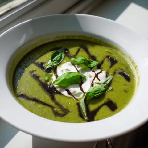 Creamy Courgette, Pea and Pesto Soup topped with crème fraîche and fresh basil in a rustic bowl.