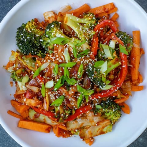Brightly colored carrots, broccoli, and sweet potato mingle with tangy kimchi in a skillet of Comforting Fermented Veggie Winter Stir-Fry, ready to garnish with sesame seeds.  