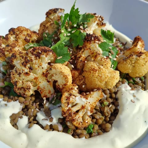 A close-up shows caramelized cauliflower and vibrant lentils, garnished with sesame seeds and parsley on a rustic platter.  