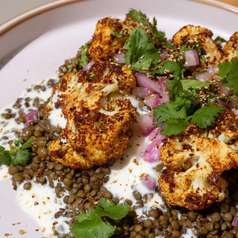 Golden roasted cauliflower florets sit atop a bed of zesty lemon lentil salad, finished with a creamy cumin-tahini yogurt drizzle and fresh herbs.  