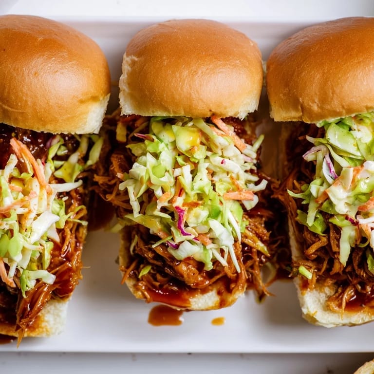 Deliciously smoky pulled pork sliders drizzled with tangy BBQ sauce and slaw.  