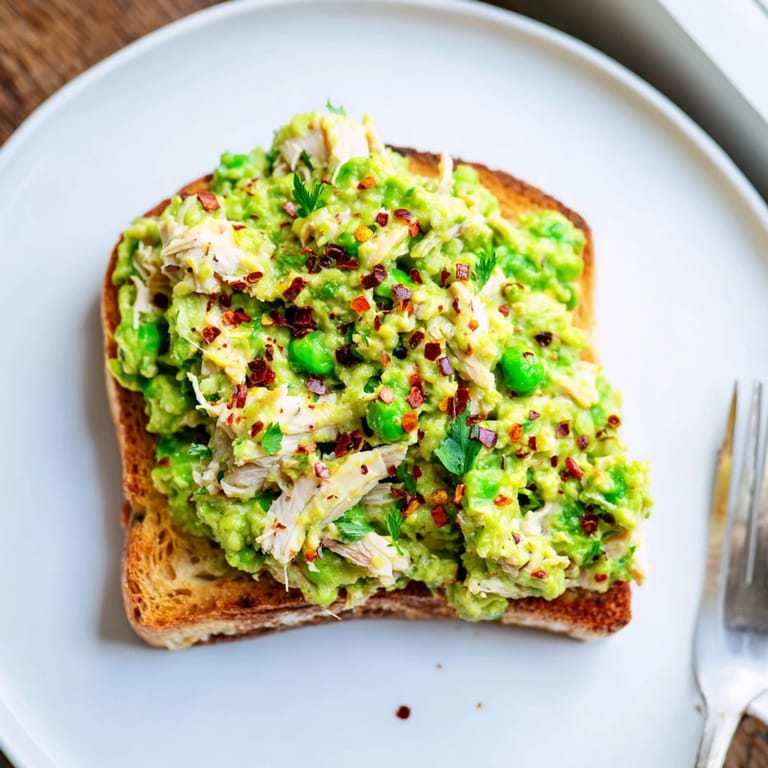 An open-faced Smashed Pea & Chicken Toast featuring a zesty lemon pea mixture, spicy chili heat, and melted feta.