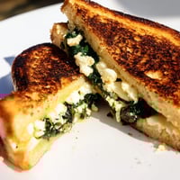 Golden-brown Feta & Spinach Stuffed Grilled Cheese slices showing melted cheese and sautéed greens oozing from thick sourdough bread.  